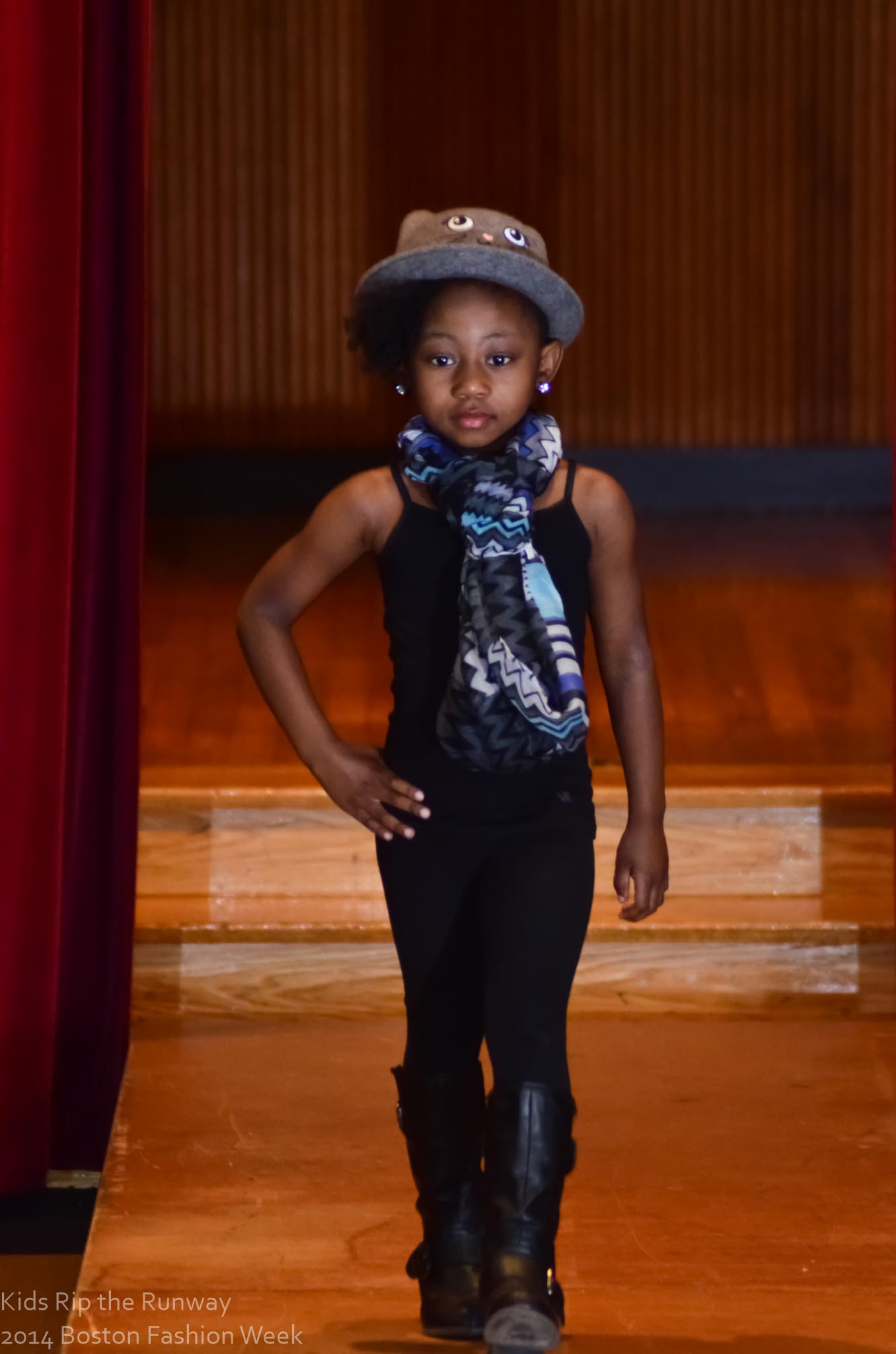 A young model walking the Kids Rip the Runway stage in a blue scarf and cap.